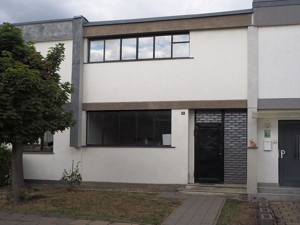 Reihenhaus in Dessau-Törten mit horizontalen Fensterbändern, weißlicher Fassade und Glasbausteinen neben der Eingangstür
